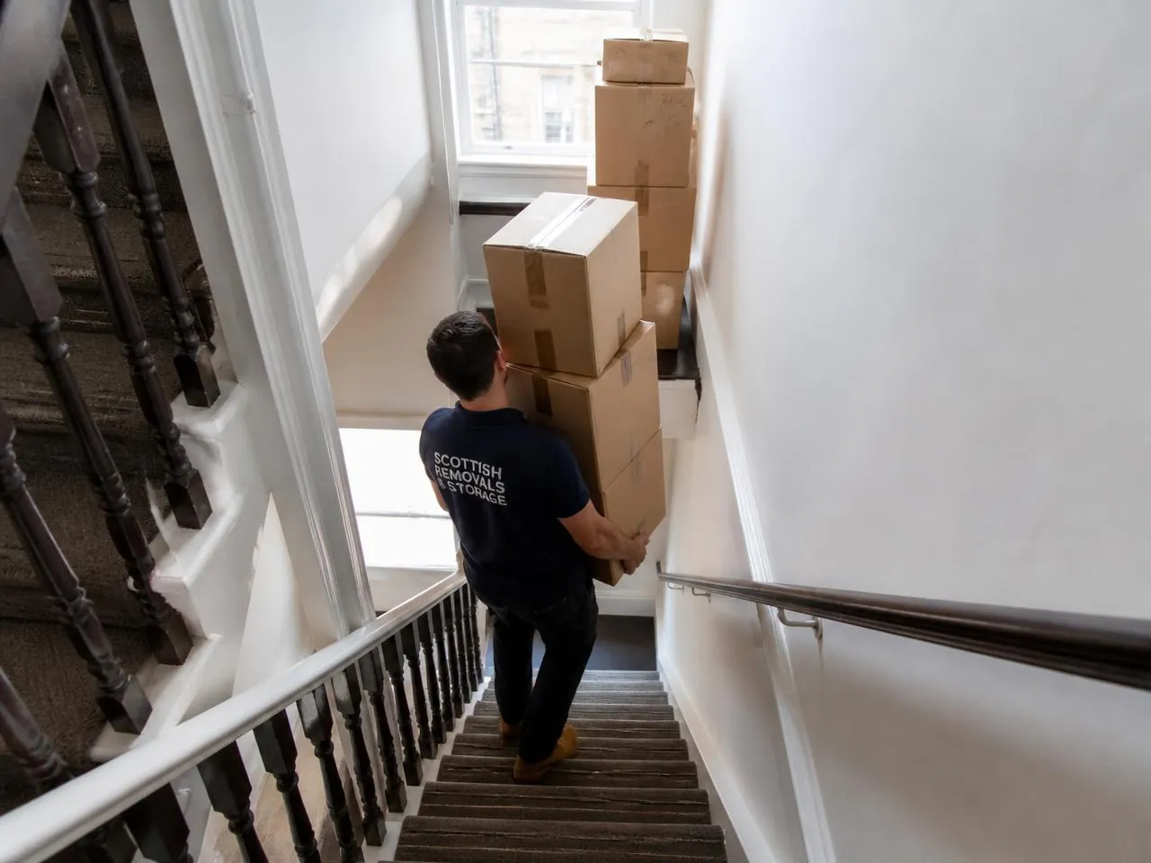 Removal worker carrying boxes down a tenement stairwell during a flat move in Lanarkshire